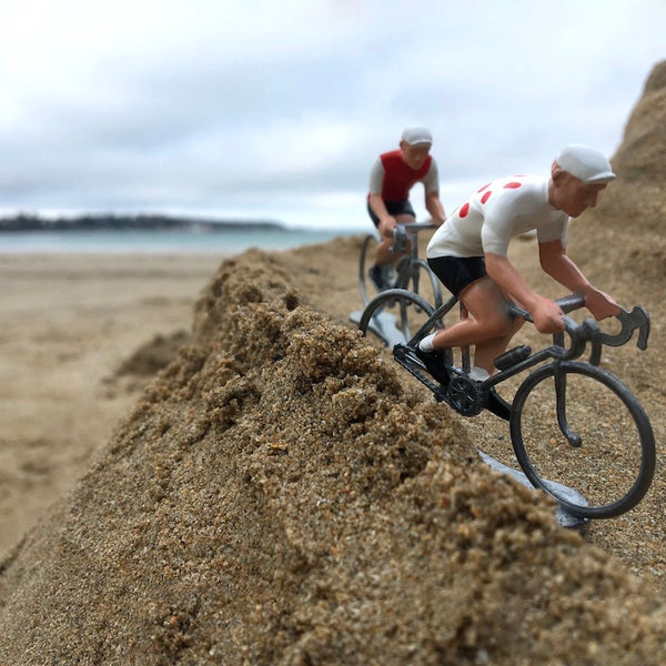 Figurines miniatures de cyclistes en métal disposées sur un parcours fait dans le sable.