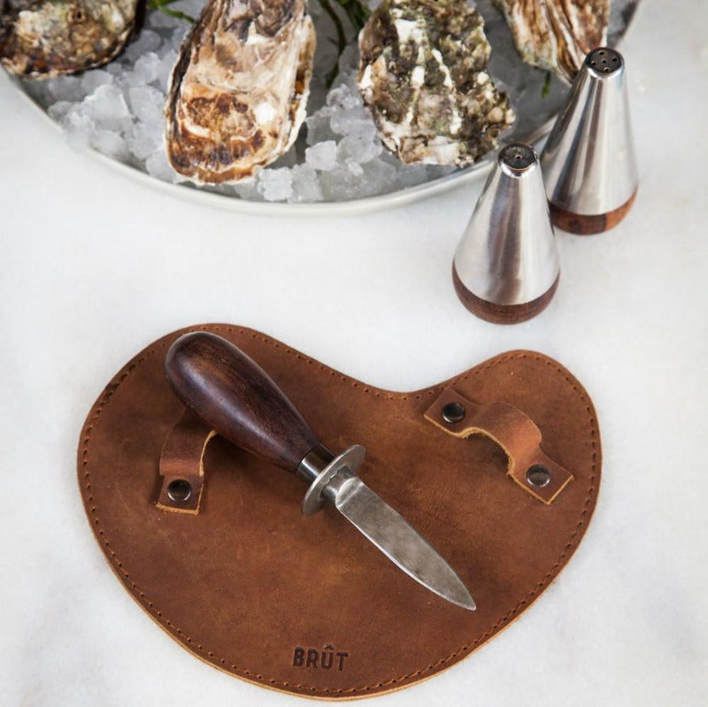 Couteau à huître avec manche en bois et lame en inox posé sur un protège main en cuir.