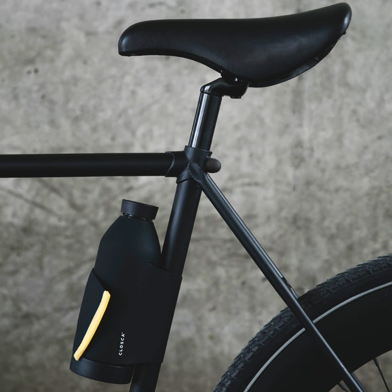 Gourde en verre noir et orange de la marque Closca accroché sur le cadre d'un vélo noir. Robin concept store masculin, boutique en ligne de cadeau pour homme. Annecy