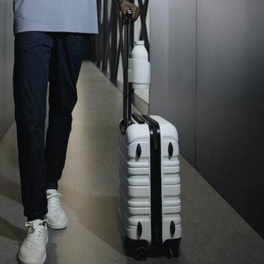 Bouteille en verre Closca Blanche fixer sur la poignet d'une valise avec le sytème de sangle incorporé sur la gourde en verre. Chez Robin concept store masculin, boutique en ligne de cadeau pour homme. Annecy